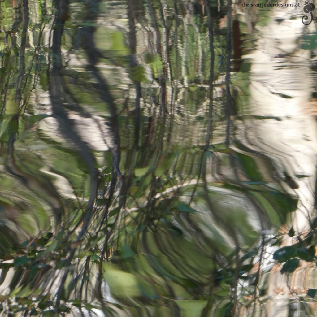 Bewegte Wasseroberfläche in der sich Bäume spiegeln.