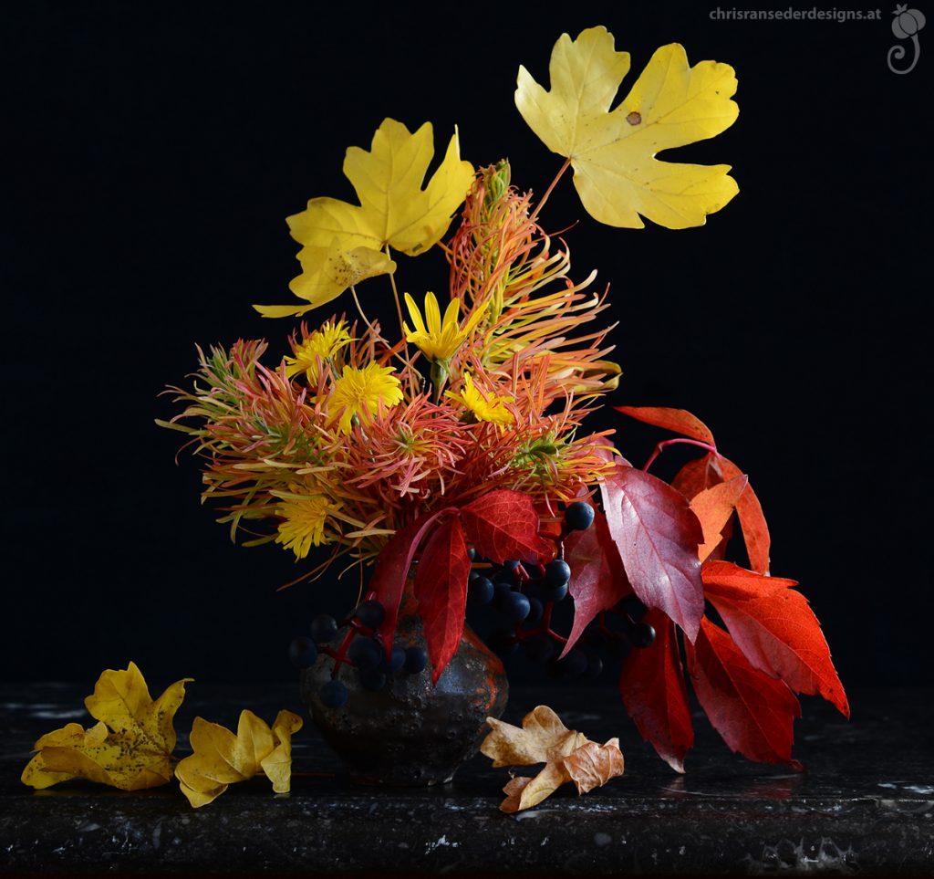 A small bouquet consisting of red and yellow foliage and yellow flowers, in a bulbous vase. | Sträußchen aus roten und gelbem Laub und gelben Blüten in einer bauchigen Vase.
