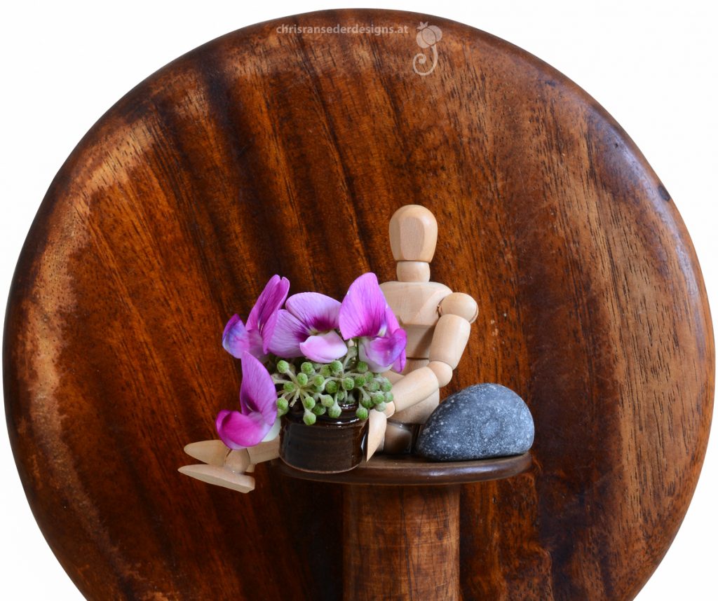 Miniatur layfigure perches atop a  thread spool and presents purple flowers in a ceramic bucket. | Mini-Gliederpüppchen, das auf einer Garnspule sitzt, reicht purpurne Blumen in einem tönernen Eimer.