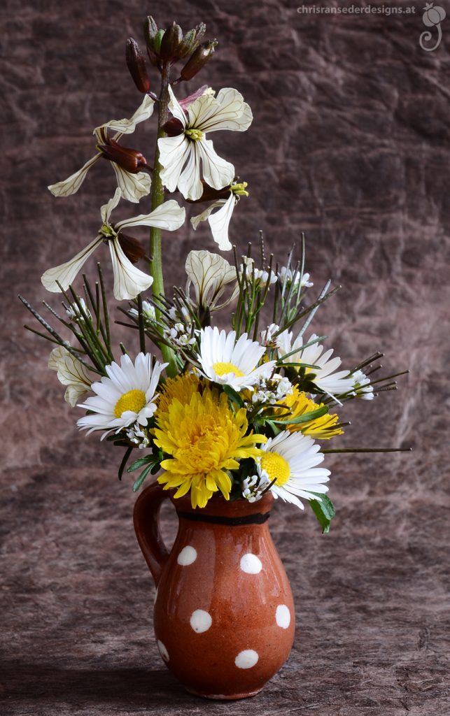 Weiße und gelbe Wiesenblumen in einem braunem Kännchen mit weißen Punkten. | White and yellow flowers in a brown pitcher with white dots.